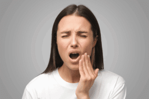 Woman holding her cheek in pain, showing signs of dental distress requiring emergency care.