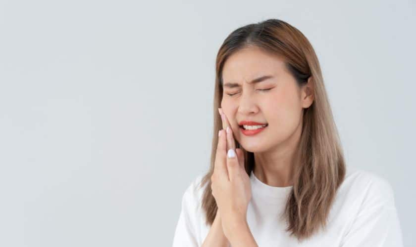 Woman touching her cheek in dental pain against white background, Prosper Smile Studio