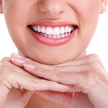 Close-up of smiling person displaying bright white teeth and healthy gums against pink background.