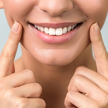 Close-up of smiling person pointing to teeth, displaying bright white smile against neutral background.