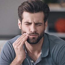 Man with beard touching his cheek in discomfort, suggesting dental pain or sensitivity.