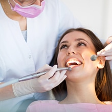 Dentist examining patient's teeth during dental checkup with mirror and tools.