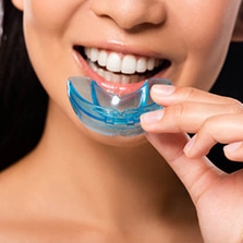 Woman inserting blue custom teeth whitening tray into her mouth for dental treatment.