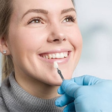 Woman smiling during dental examination with dentist holding mouth mirror in clinical setting.
