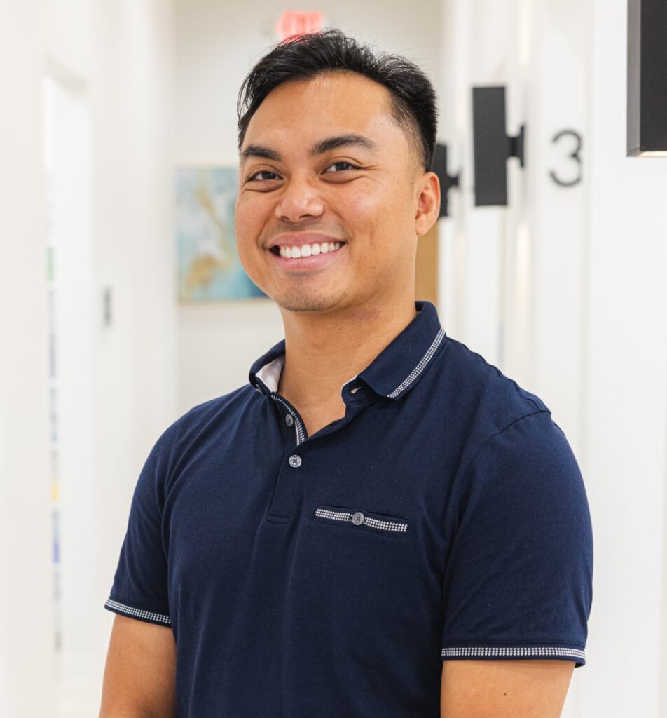 Young male dental professional smiling in navy polo shirt at modern dental office.