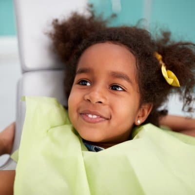 Young child smiling at dental office wearing yellow shirt with hair clips