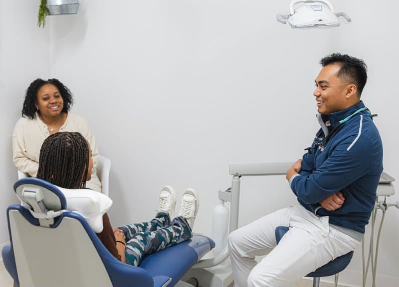 Dentist consulting with mother and child patient in bright dental office treatment room.