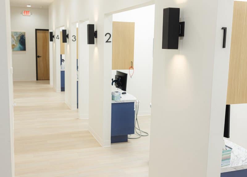 Modern dental office hallway with treatment rooms, numbered doors, and contemporary white and wood interior design.