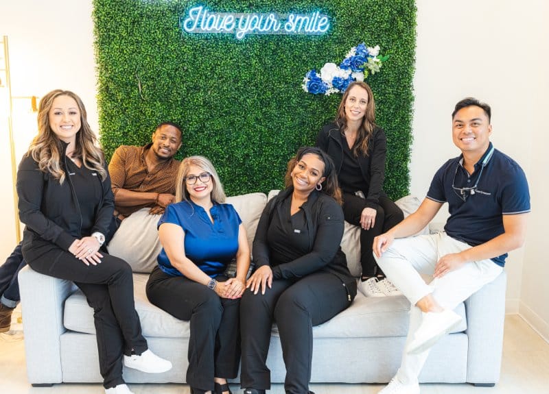 Prosper Smile Studio dental team of six professionals posing together in modern office with green living wall.