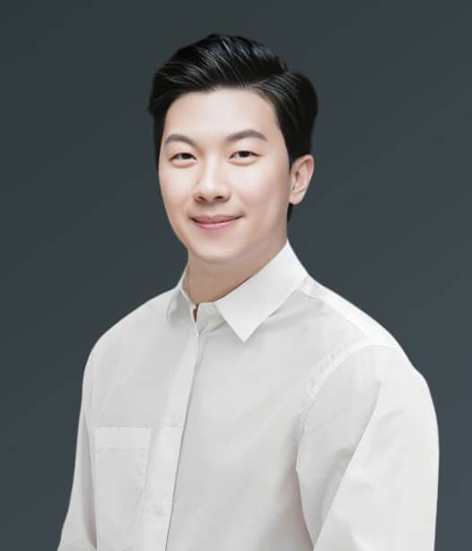 Professional headshot of Asian male dentist wearing white shirt against gray background.