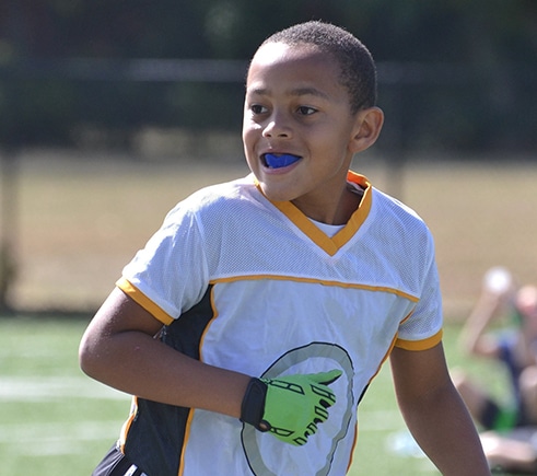 Young athlete wearing blue sports jersey with blue mouthguard on outdoor field.