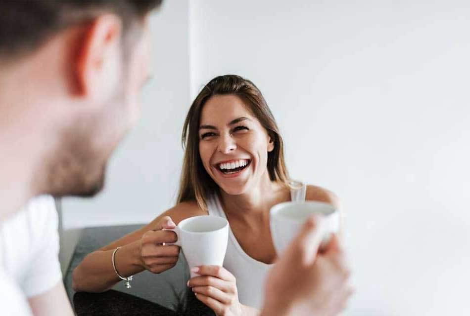 Two people enjoying coffee together in a bright, modern dental office setting, smiling.