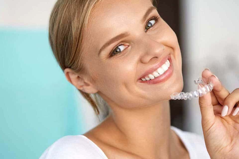 Woman brushing teeth and smiling at camera in dental office setting.