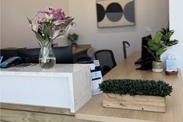 Modern dental office reception desk with flowers, plants, and welcome amenities on wooden counter.