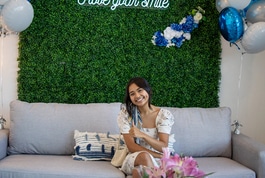 Woman sitting on couch holding dental model in modern dental office setting with green wall backdrop.