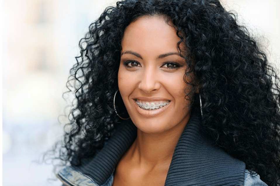 Professional headshot of smiling woman with curly black hair wearing dark blazer against blurred background.