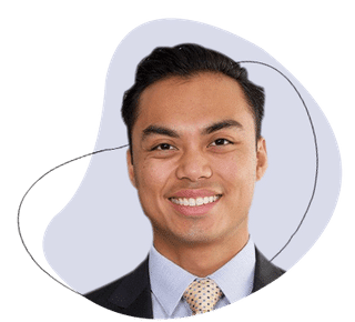 Professional headshot of smiling male dentist in business suit against light blue background.