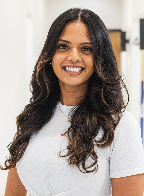 Young woman smiling at camera in dental office setting, wearing white shirt.