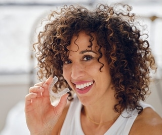 Woman with curly hair smiling while holding dental floss in bright dental office setting.