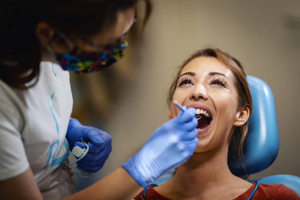 Dentist in blue gloves examining patient's teeth in dental clinic chair.