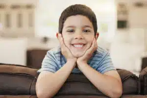Smiling young boy with hands on cheeks in blue striped shirt at dental office.