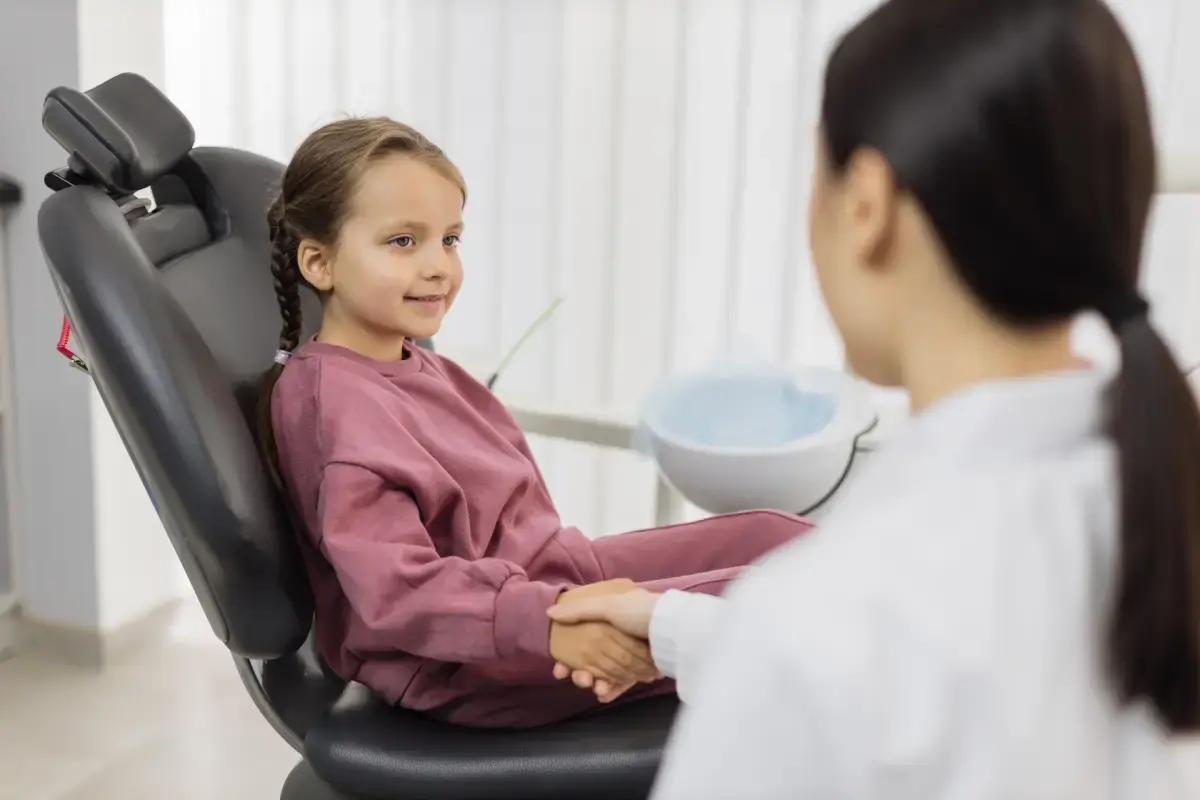 Young patient in dental chair smiling at dentist during checkup visit.